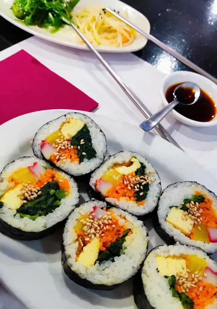 Rollos de sushi en un plato blanco con salsa de soja y palillos sobre una mesa de restaurante.