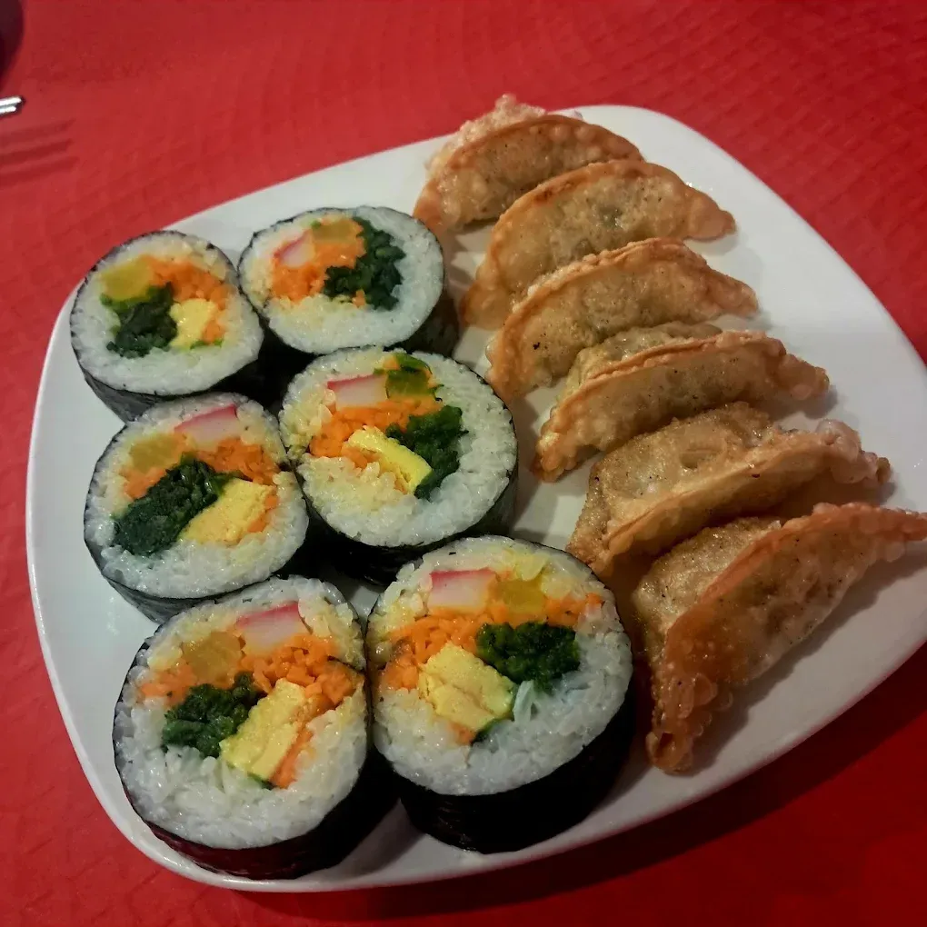 Plato de rollitos de sushi y empanadillas a la plancha sobre un mantel rojo