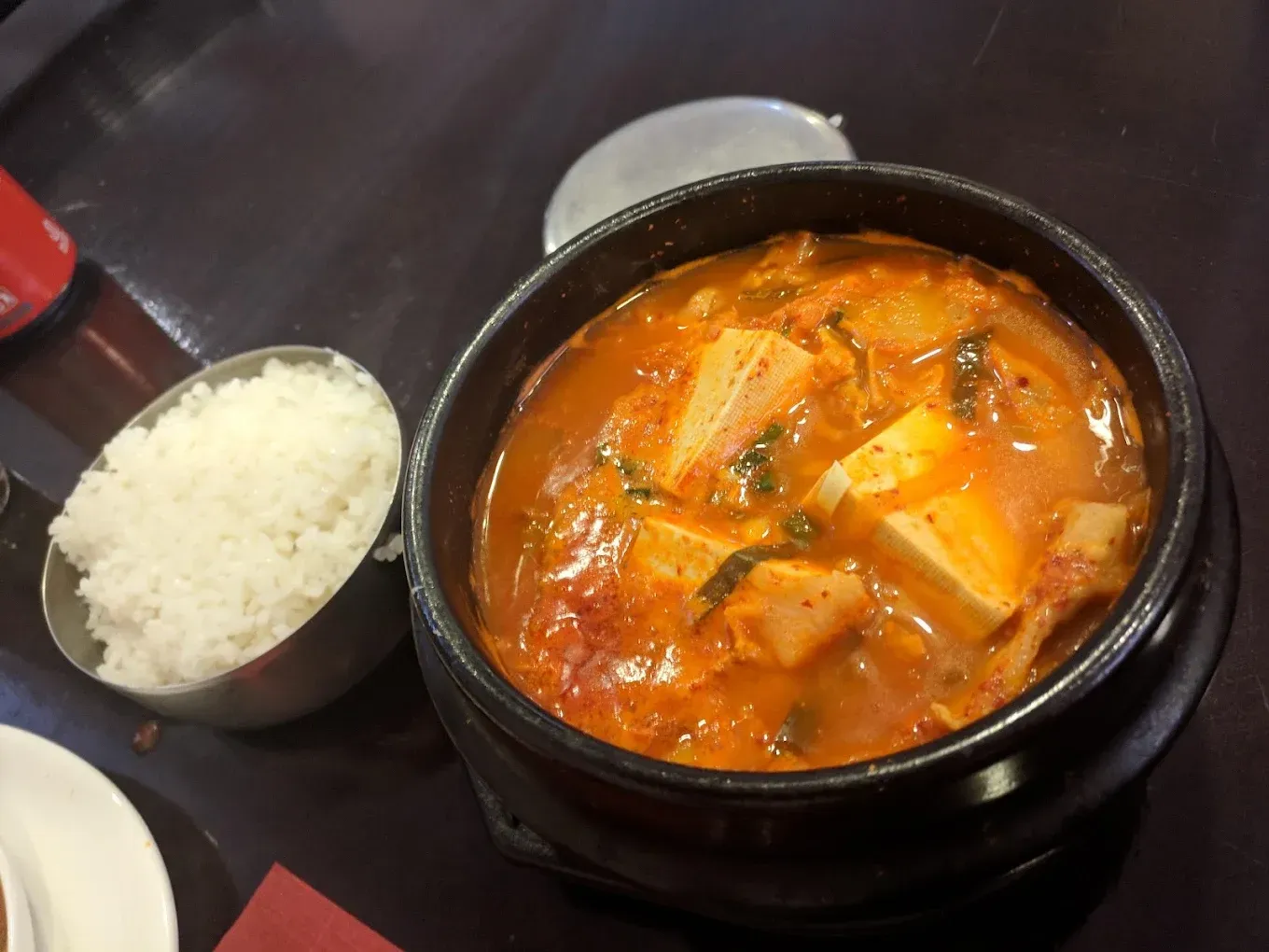 Guiso coreano en una olla negra con tofu y verduras, servido con un cuenco de arroz blanco sobre una mesa