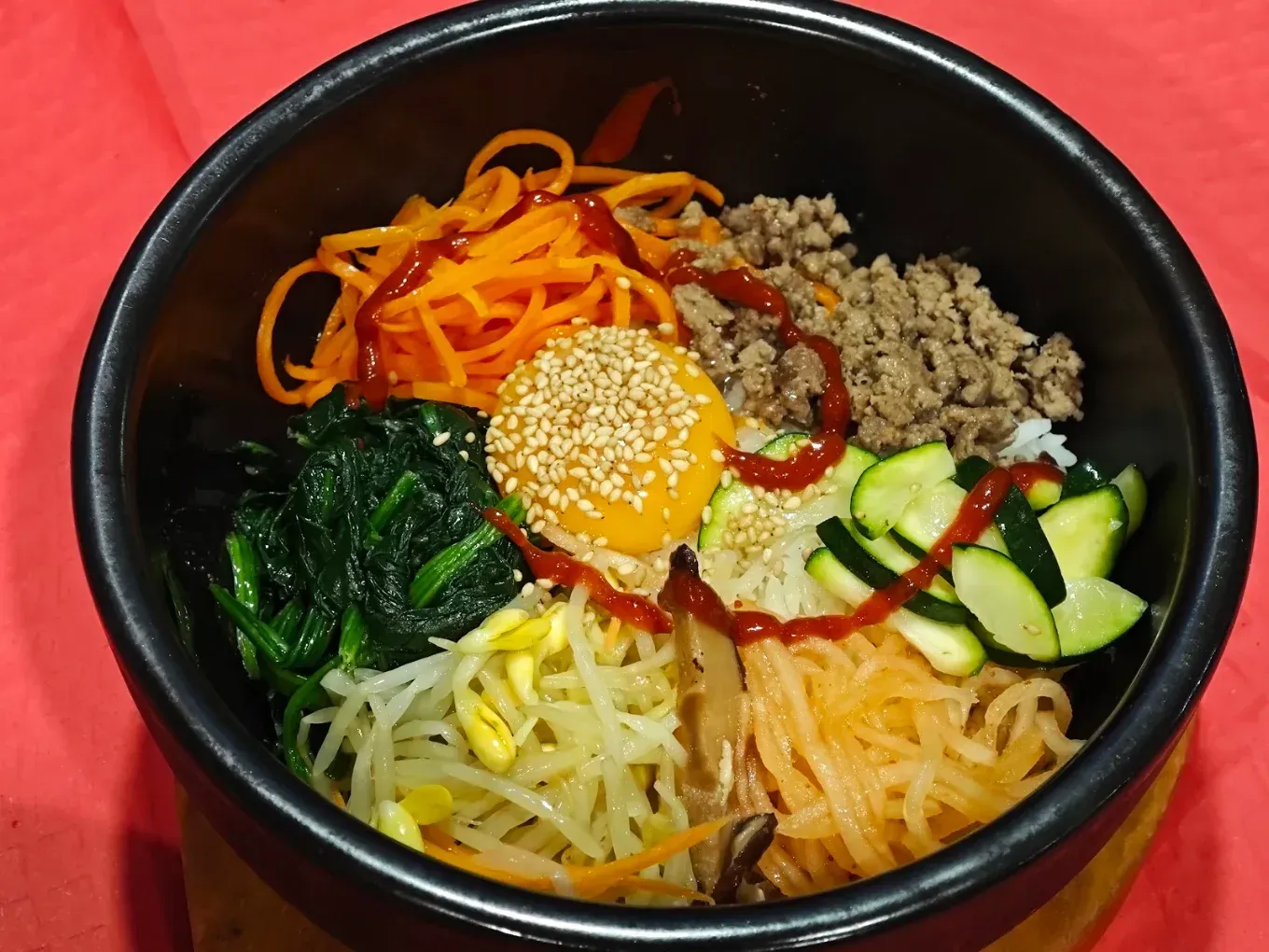 Bibimbap en un cuenco negro con verduras de colores, ternera y una yema de huevo cruda sobre una mesa roja