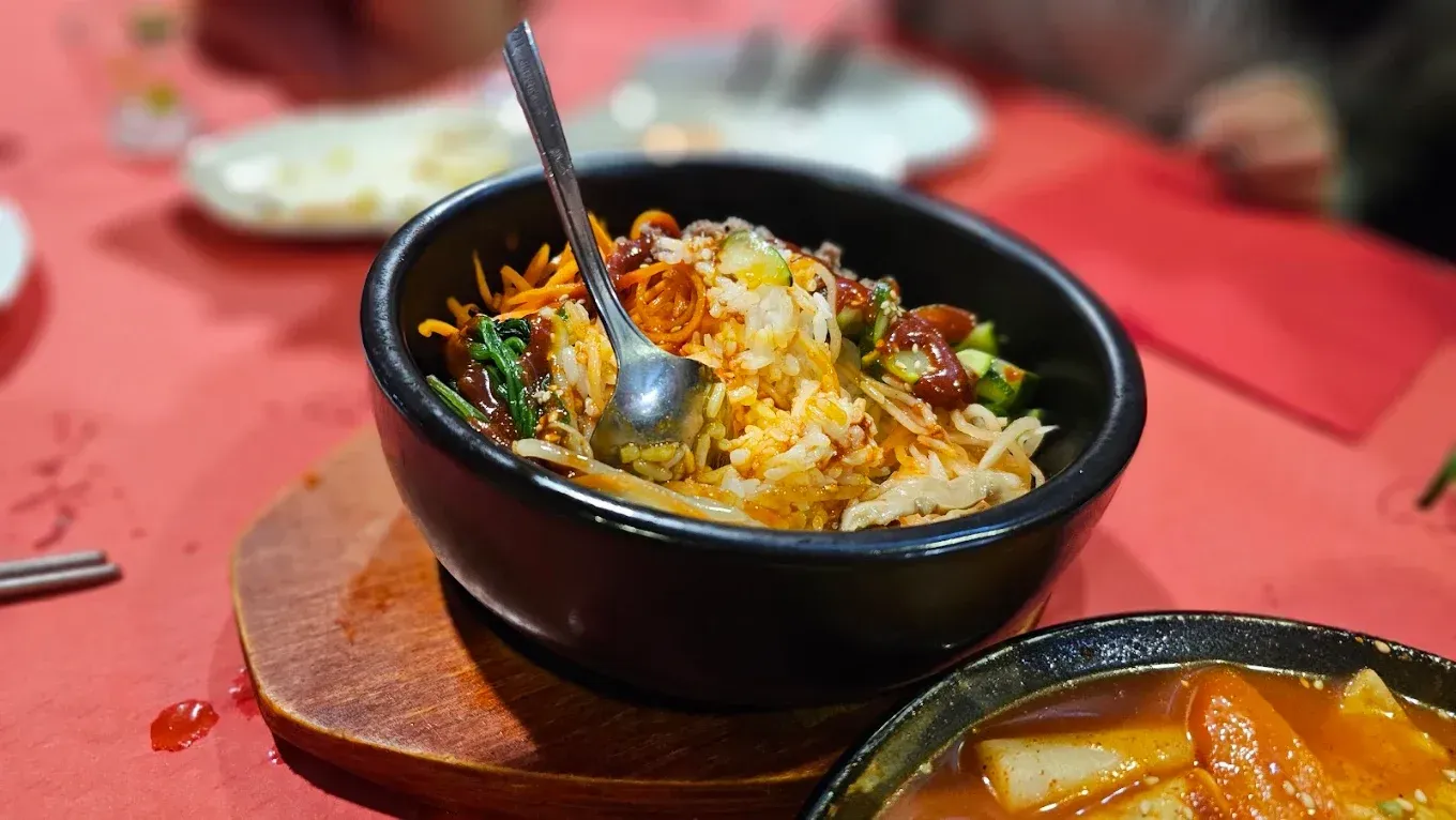 Bol negro de arroz con una cuchara sobre un mantel rojo, con un pequeño cuenco de sopa cerca