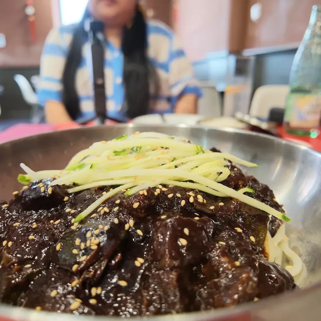 Primer plano de fideos oscuros con salsa, cubiertos de pepino rallado, en un cuenco metálico sobre la mesa de un restaurante