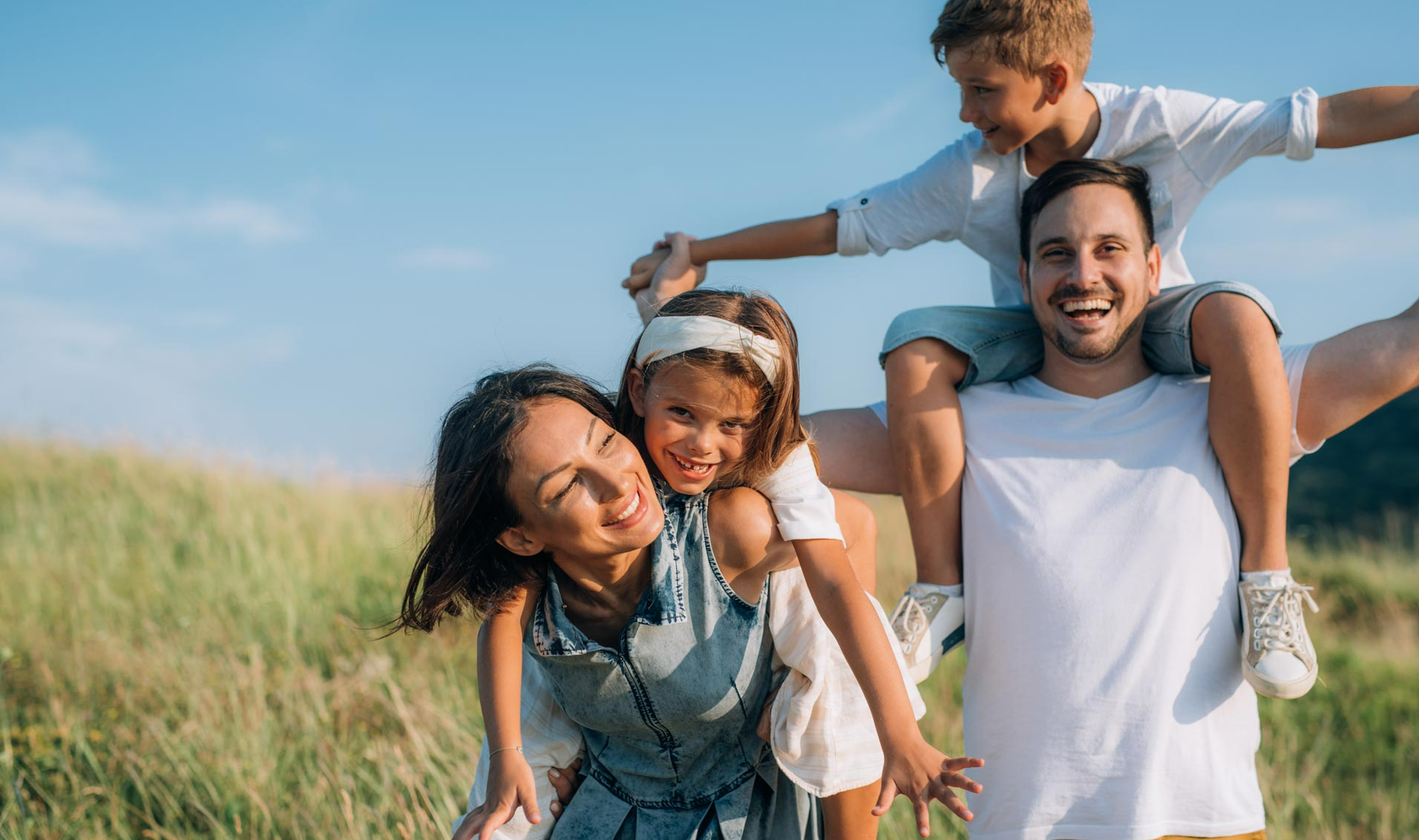 Parents heureux qui portent leurs enfants sur leurs dos dans un champs verdoyant
