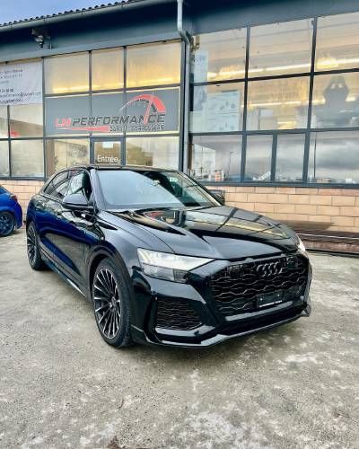 Une audi q8 noire est garée devant un immeuble.