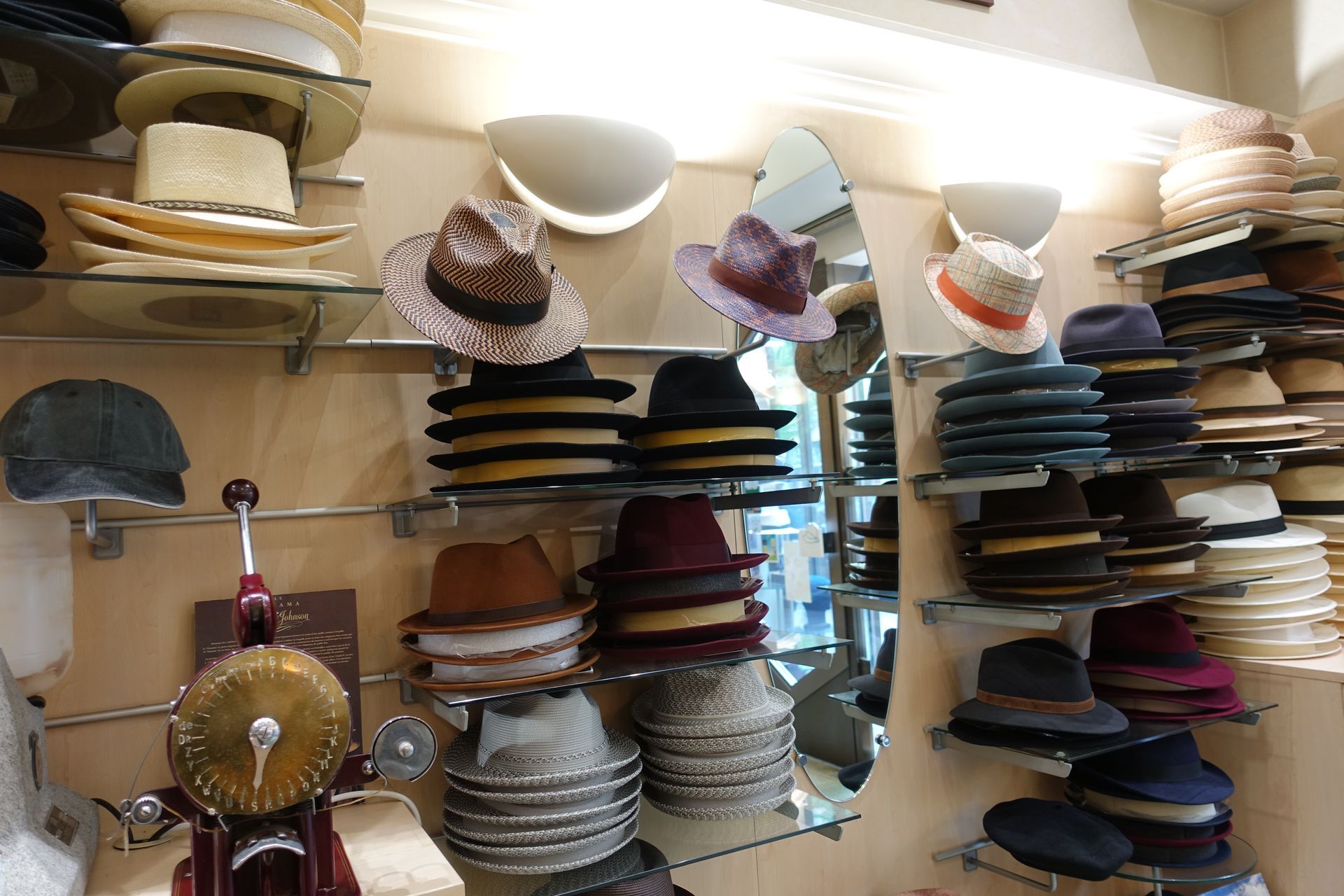 Des étagères remplies de chapeaux dans une boutique, avec un petit gong en laiton et un miroir au centre.