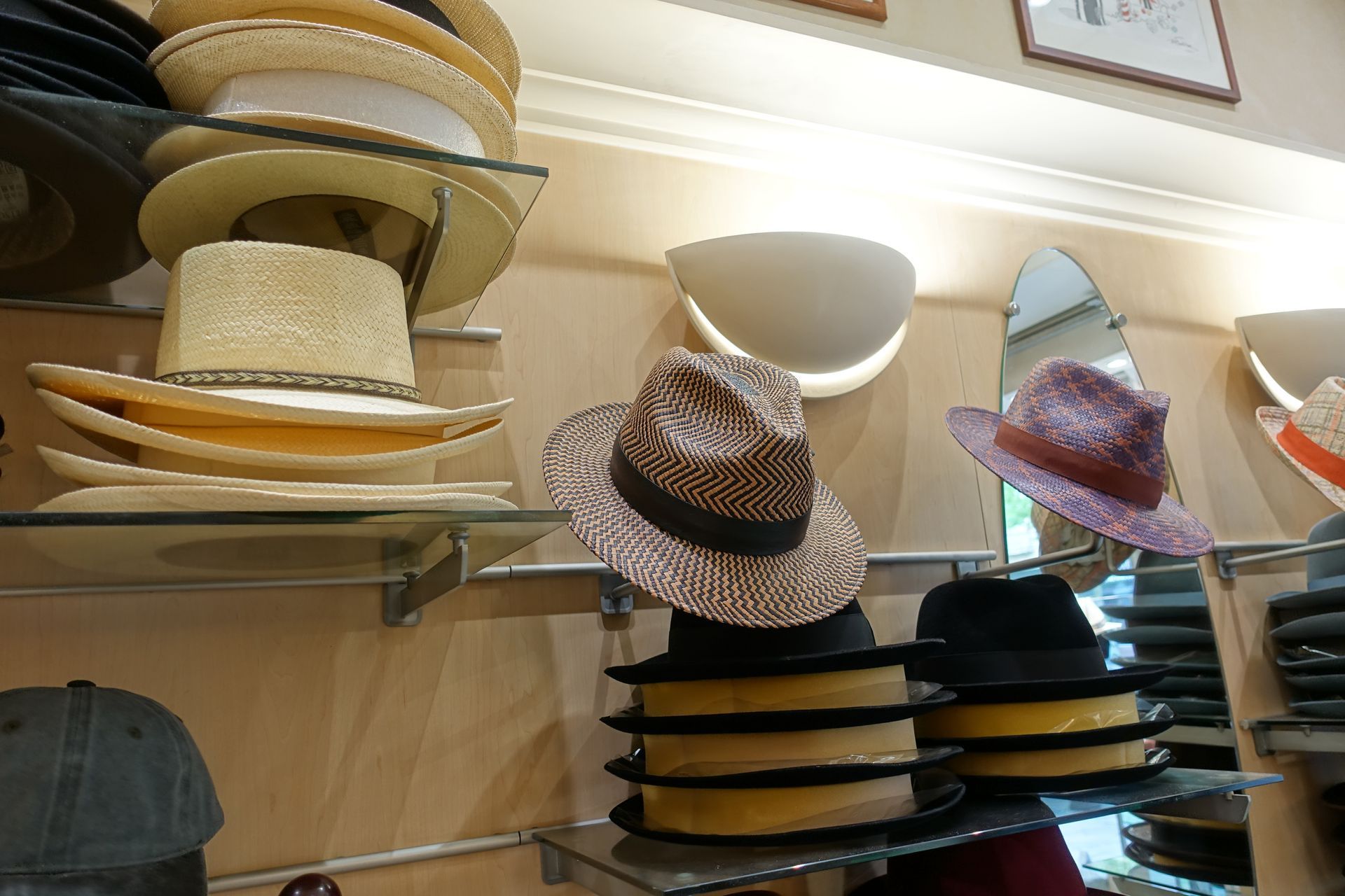 Des chapeaux de paille et de paille tressée sont présentés sur des étagères et des présentoirs muraux dans un magasin, notamment des modèles noirs, beiges et roses.