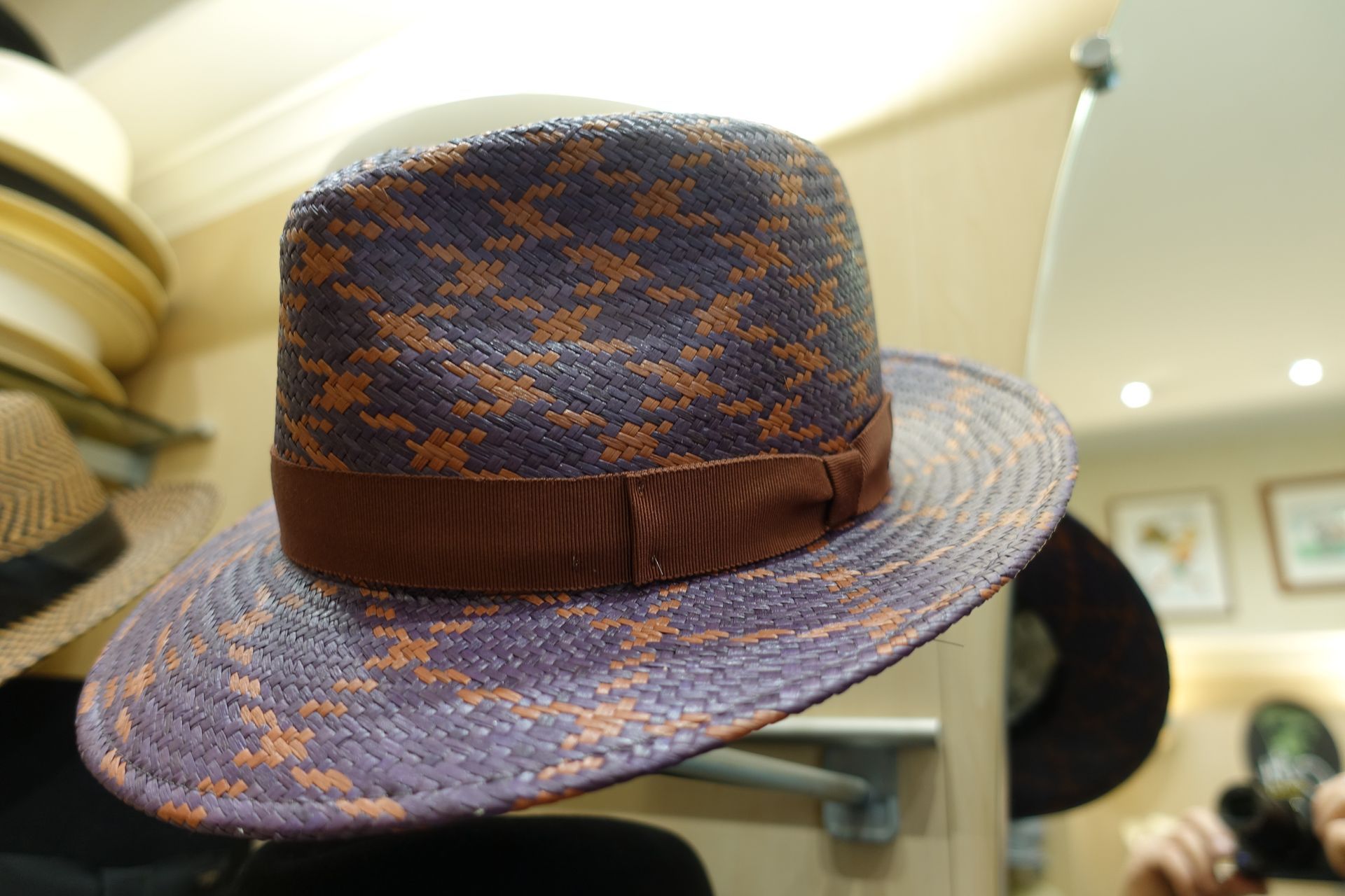 Un chapeau Fedora bleu à motifs avec un ruban marron est exposé sur une étagère dans un magasin.