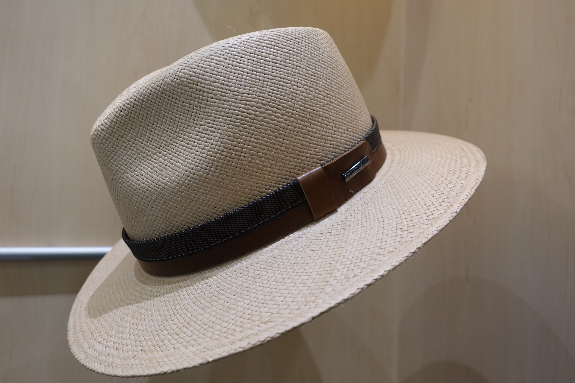 Chapeau fedora en paille beige avec un ruban marron, présenté sur un fond en bois uni