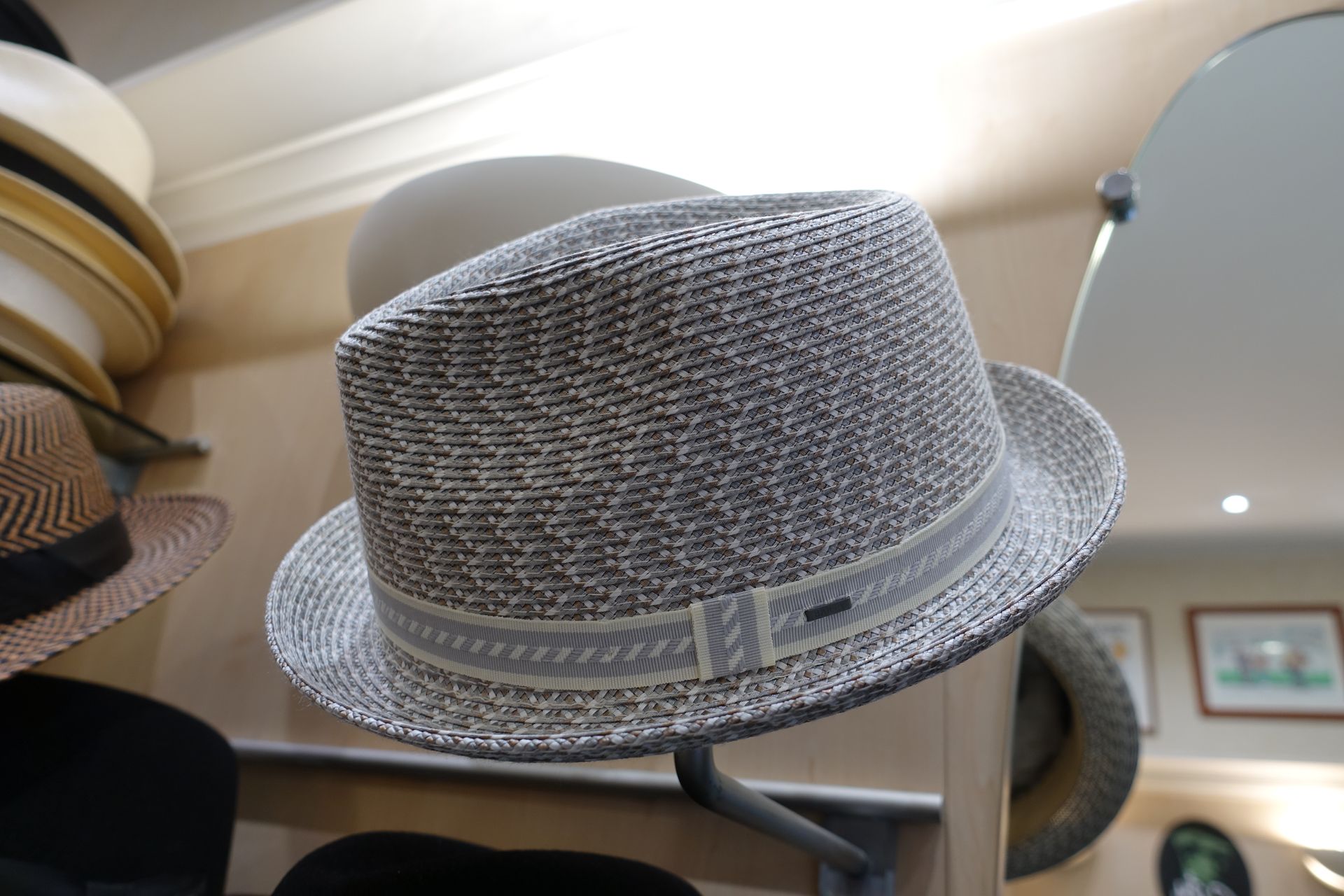Fedora gris tissé avec ruban exposé sur un présentoir à chapeaux dans un magasin