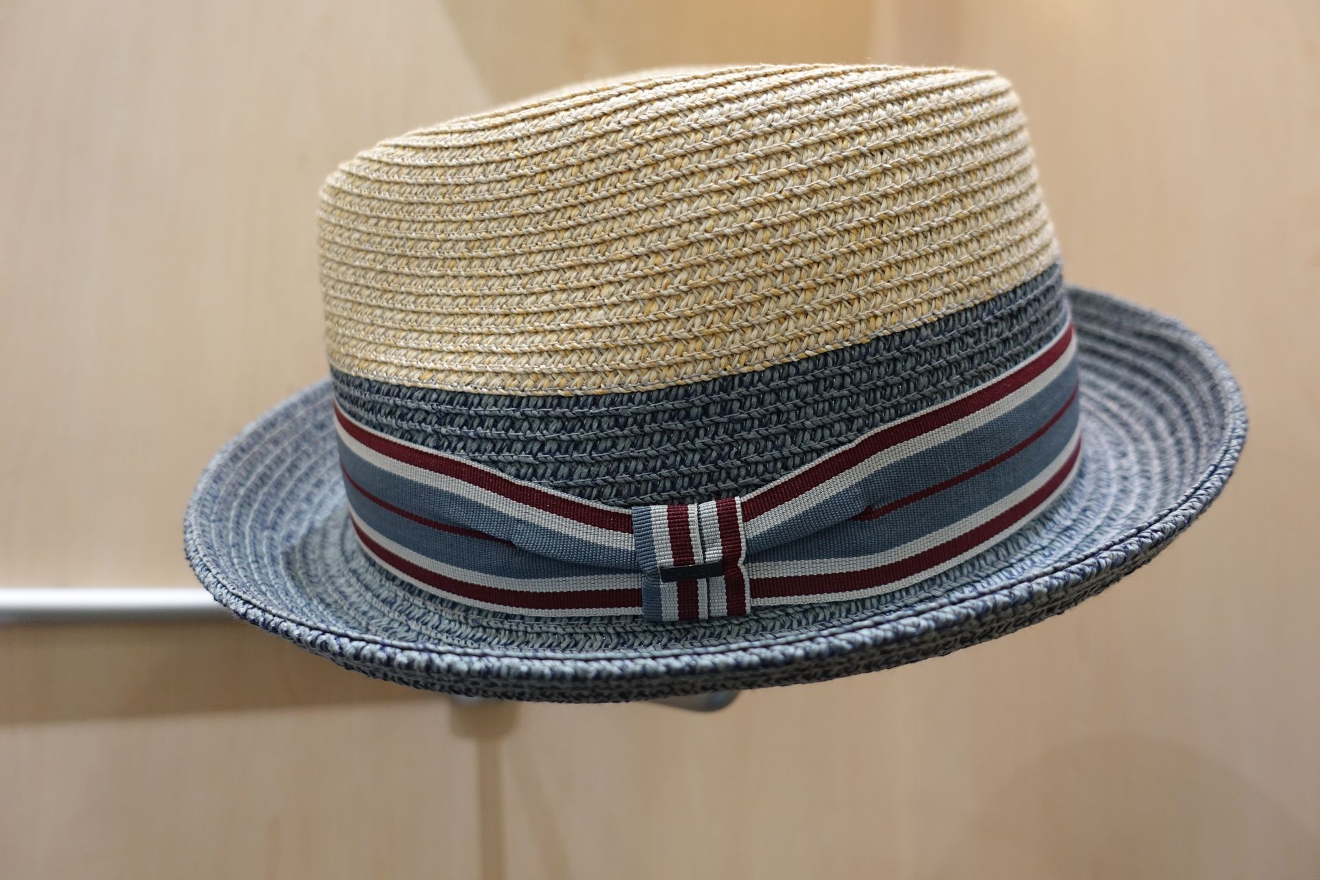 Canotier en paille avec un bandeau rayé bleu et rouge sur fond beige uni
