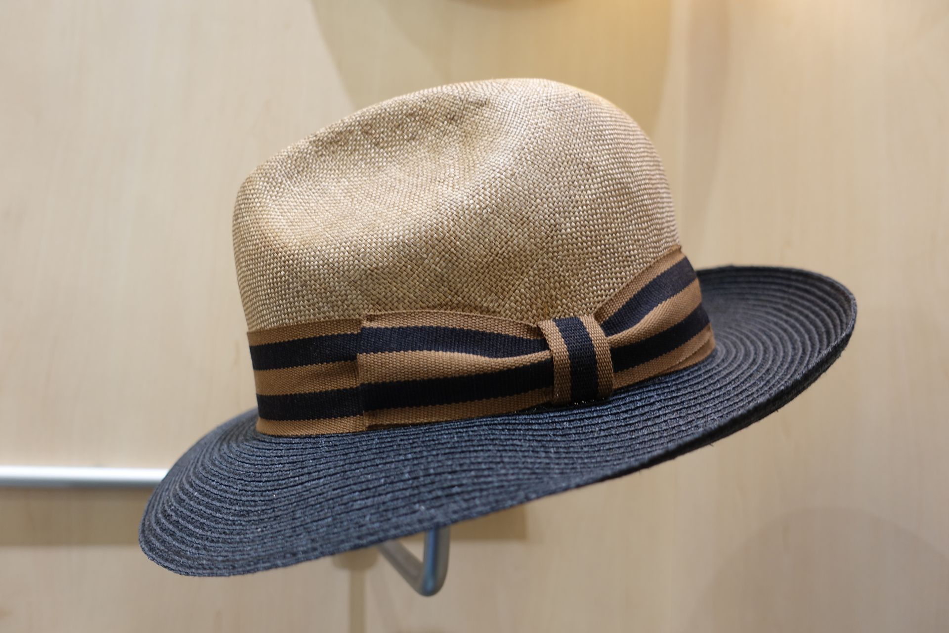 Chapeau de paille à bord bleu marine et ruban, accroché à un crochet mural