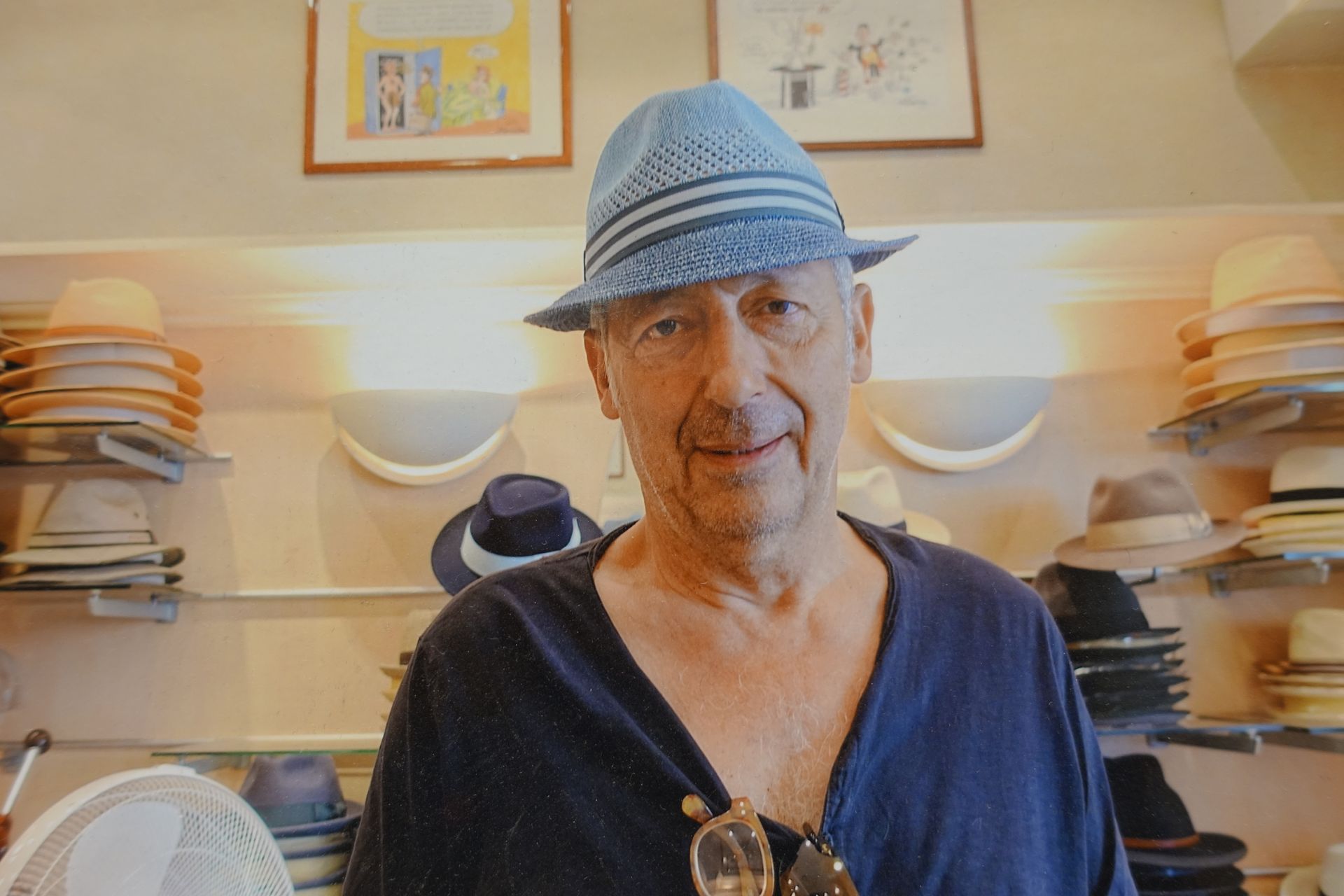 Une personne portant un chapeau bleu se tient dans une chapellerie entourée de chapeaux empilés et d'appliques murales.