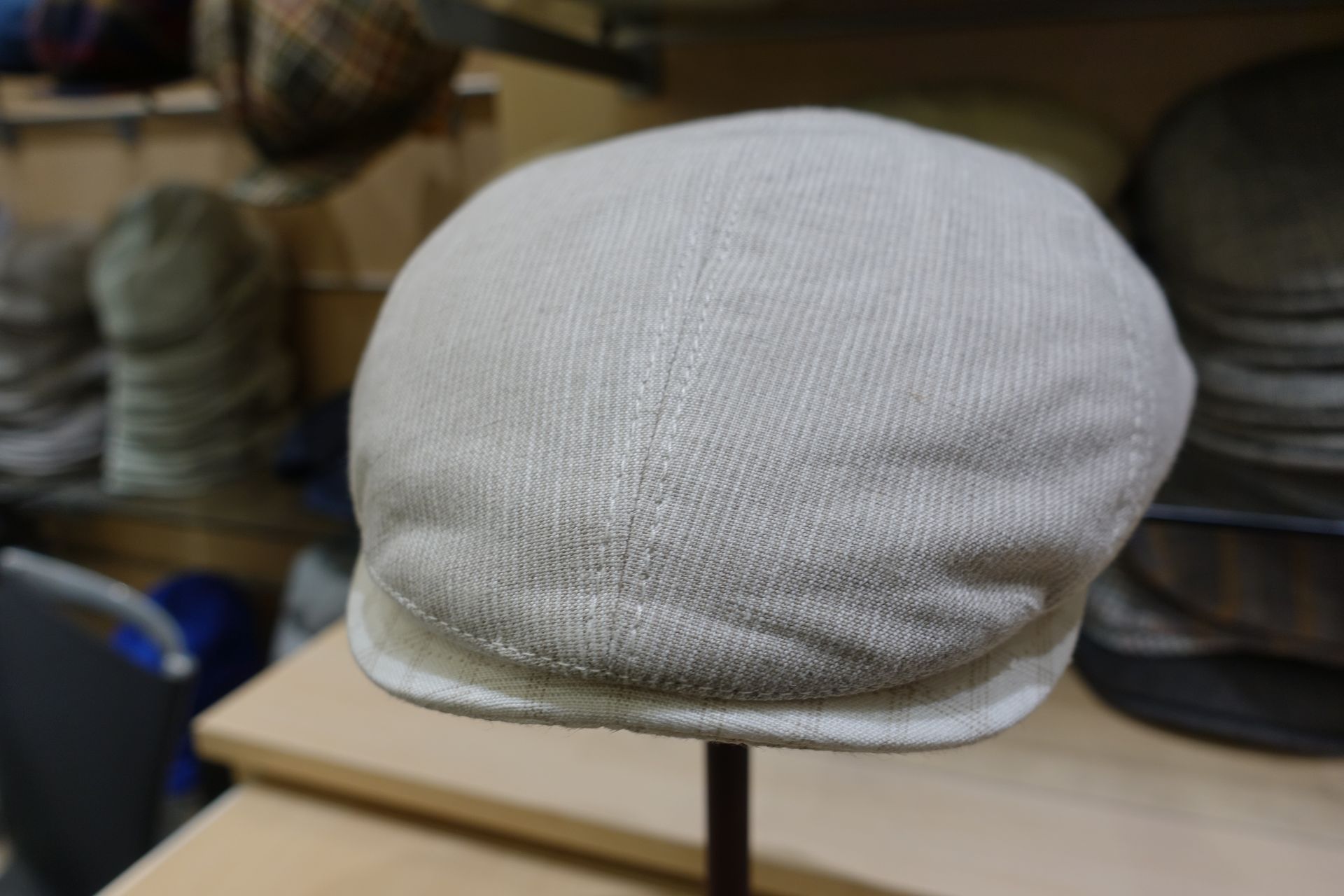 Béret en maille gris clair sur un présentoir, avec des étagères floues en arrière-plan.