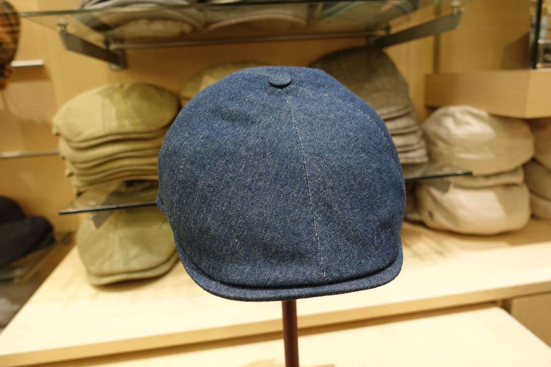 Béret présenté sur un présentoir dans un magasin, avec des chapeaux empilés sur des étagères derrière.