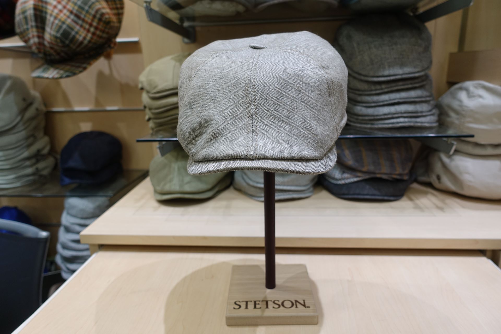 Chapeau Stetson gris sur un présentoir, avec d'autres chapeaux sur des étagères derrière.