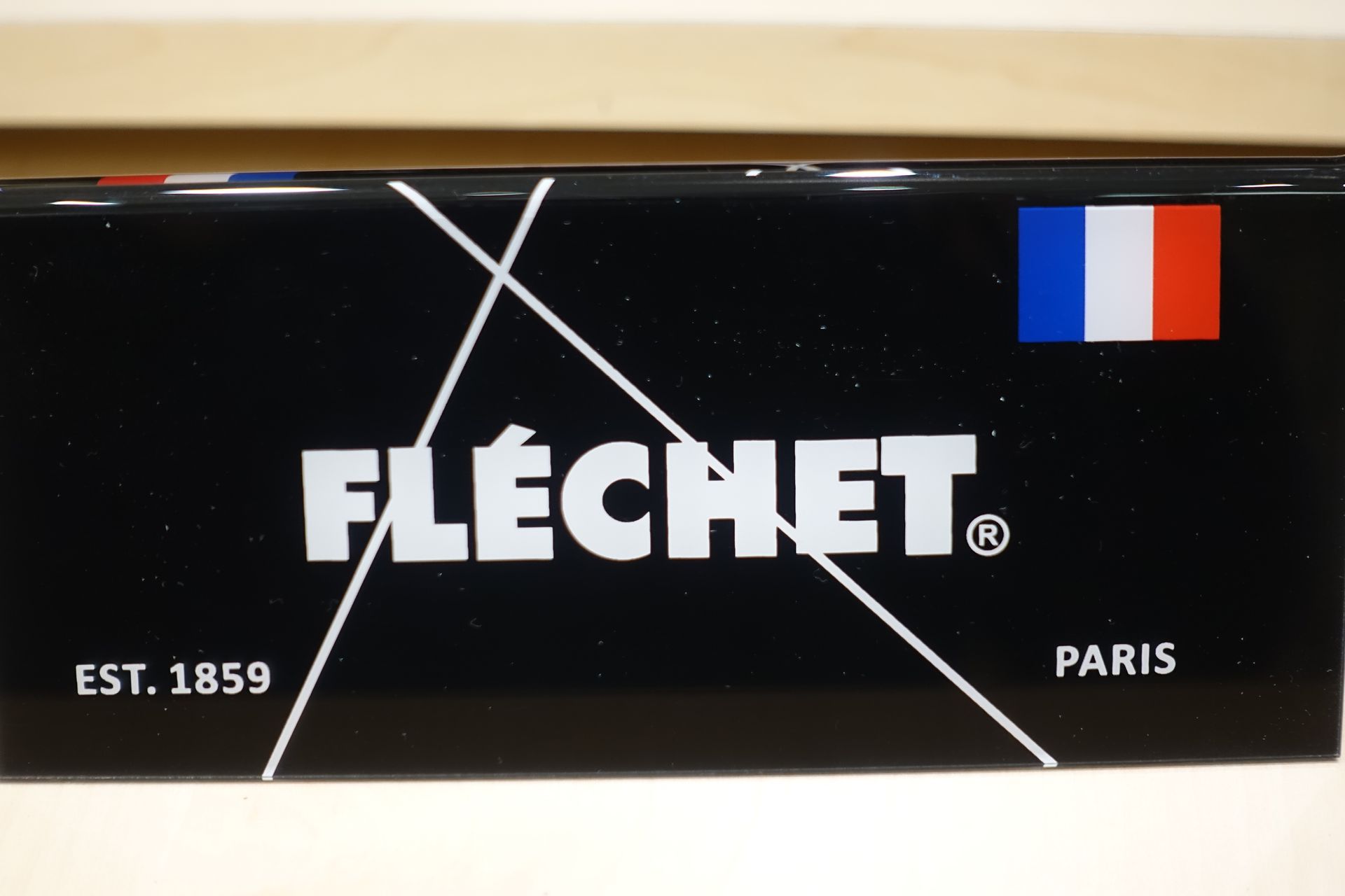 Enseigne Fléchet noire avec logo blanc, « EST. 1859 » et « PARIS », et drapeau français dans le coin