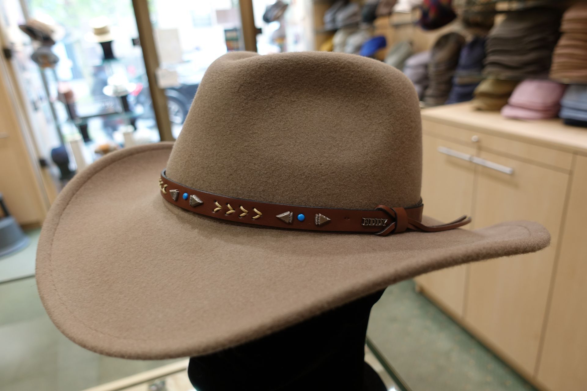Chapeau de cowboy en feutre beige avec un ruban de perles marron, exposé dans une chapellerie.