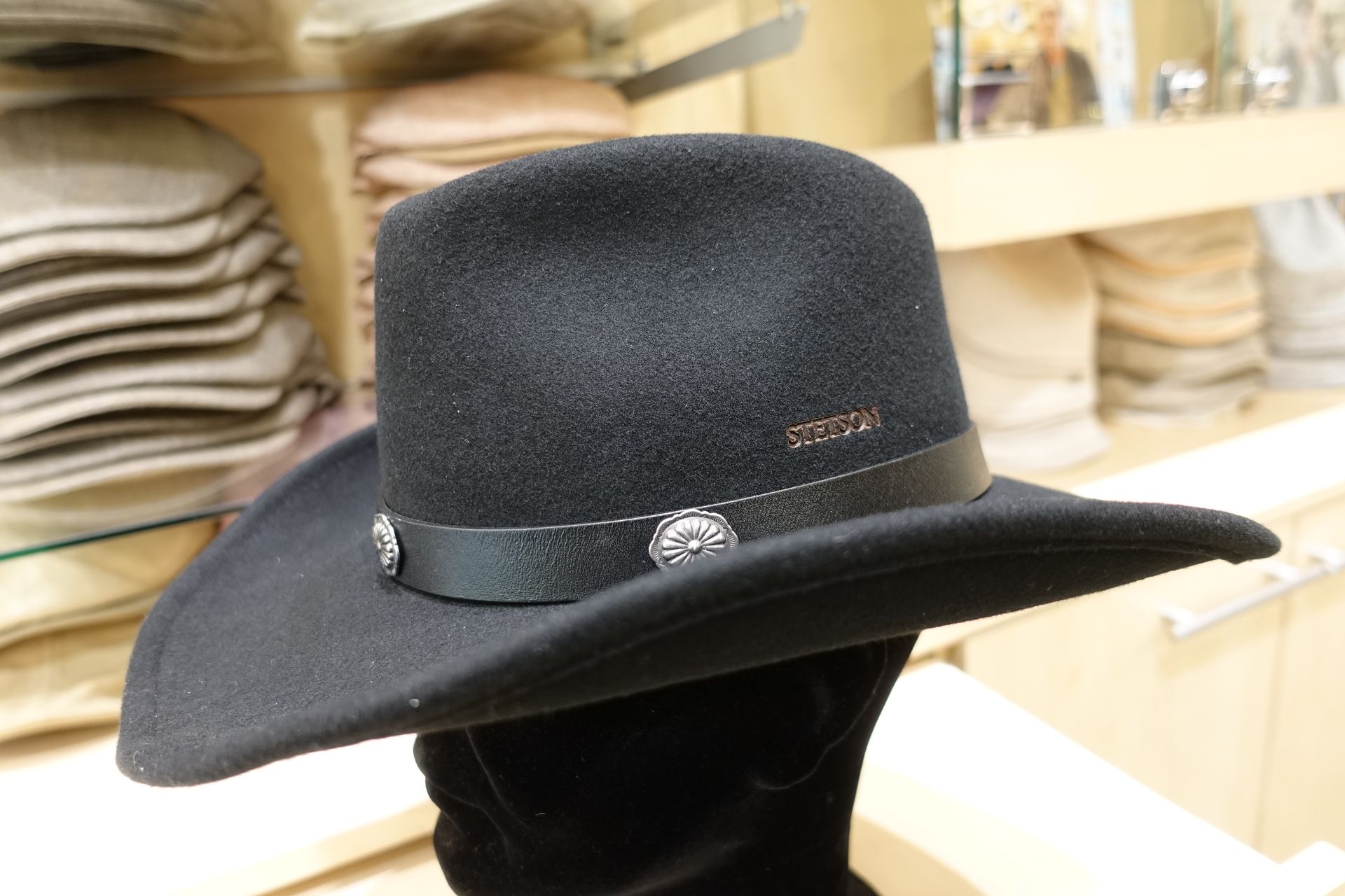 Chapeau noir en feutre à larges bords avec un ruban, exposé sur une étagère dans un magasin.