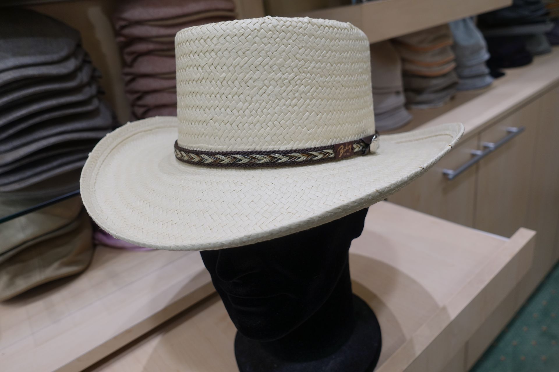 Chapeau de cowboy blanc tissé avec un ruban noir, présenté sur un présentoir noir dans un magasin.