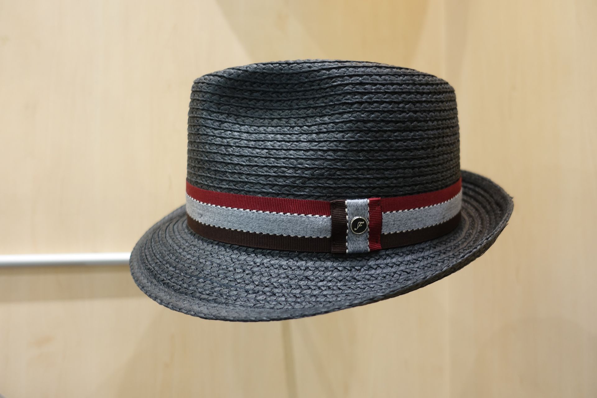 Fedora noir tissé avec un bandeau rouge et gris sur fond de bois clair