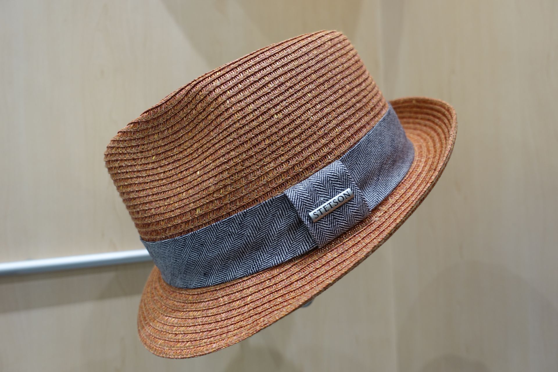 Chapeau tissé marron avec un ruban et un nœud bleus, présenté devant un mur clair.