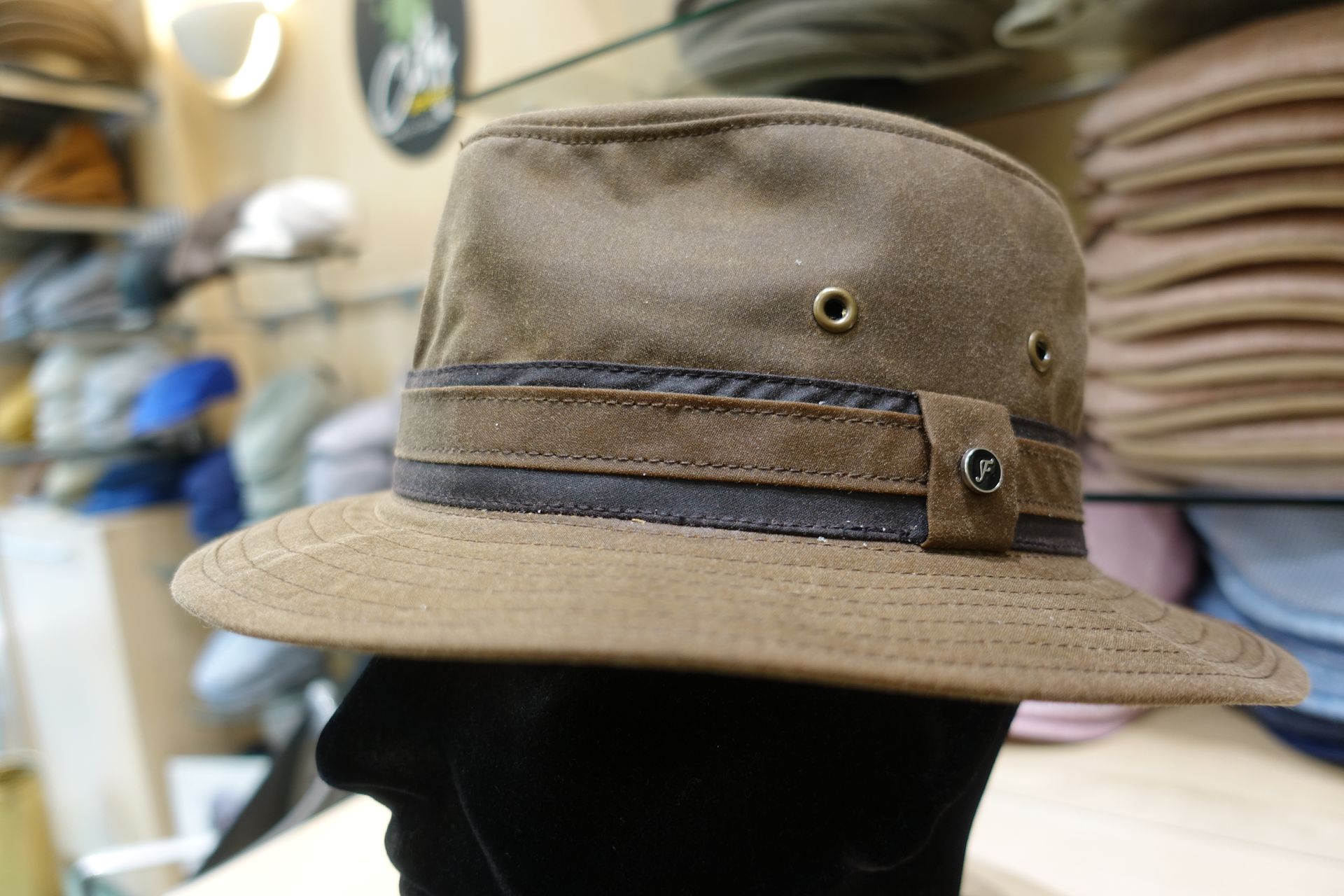 Chapeau fedora beige avec un bandeau foncé et un bouton décoratif, présenté sur une tête de mannequin