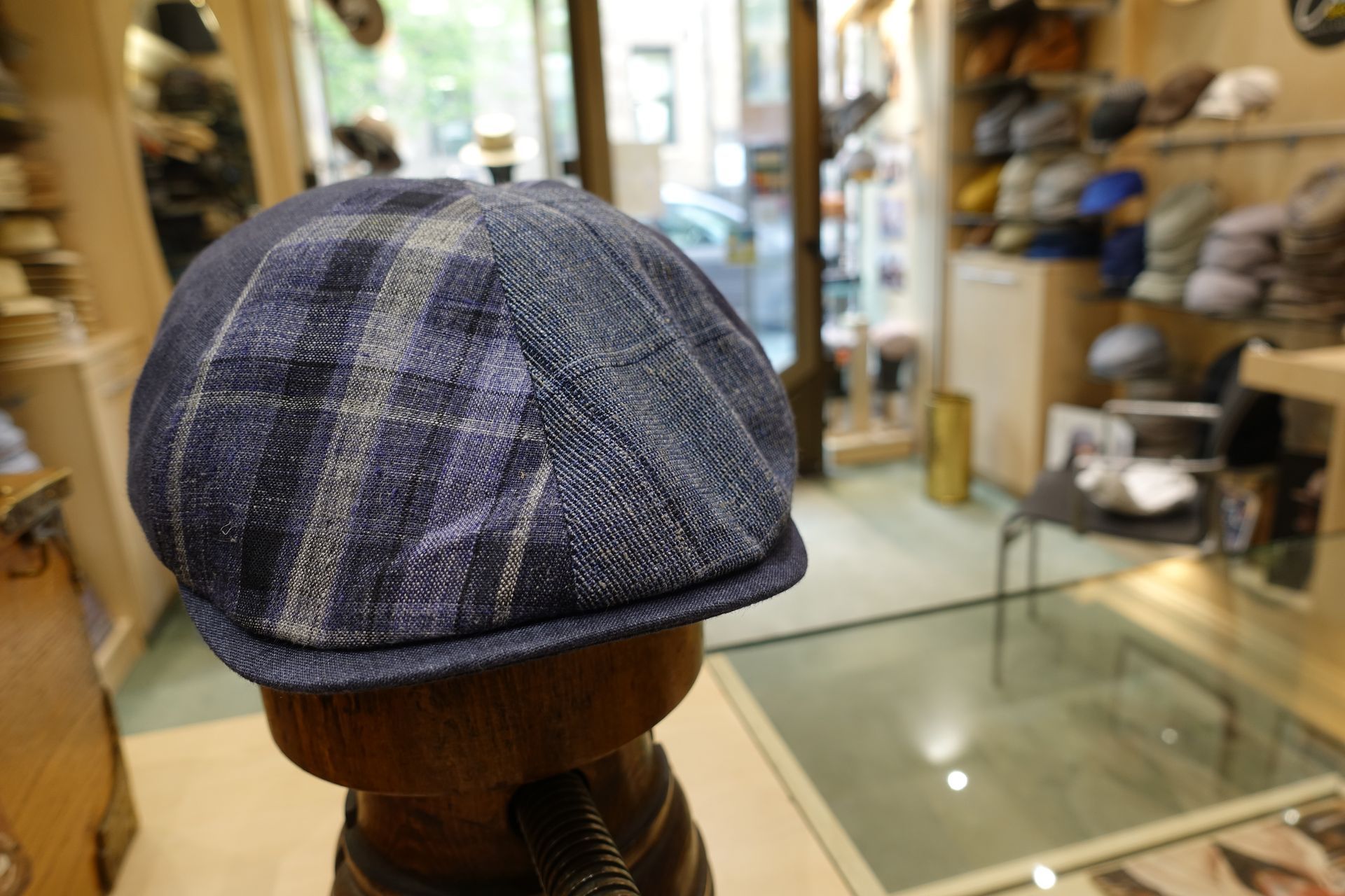 Casquette plate à carreaux bleu-gris sur un support en bois dans une vitrine de magasin