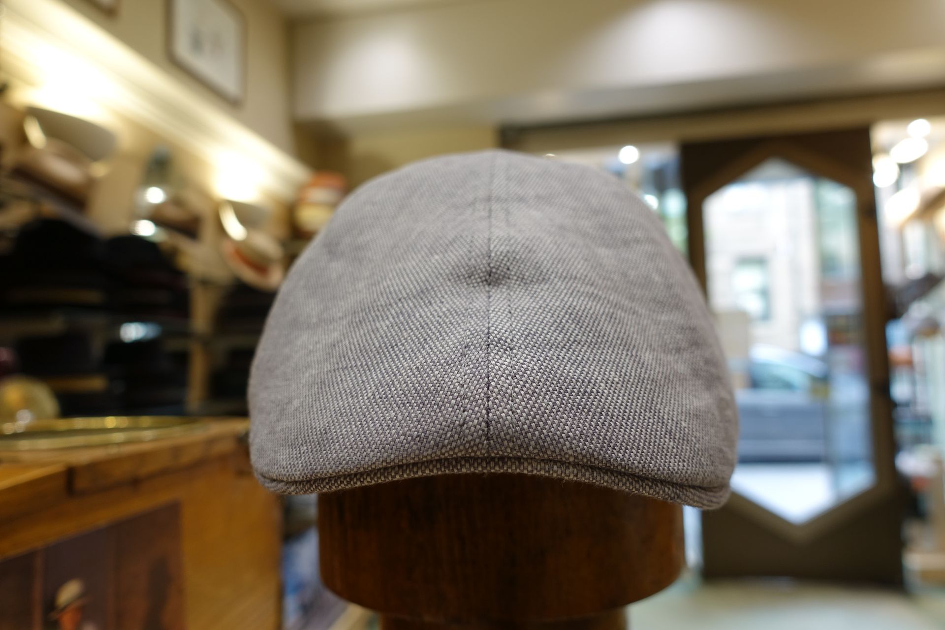 Béret gris tricoté sur un mannequin en bois dans l'intérieur d'un magasin à l'éclairage tamisé.