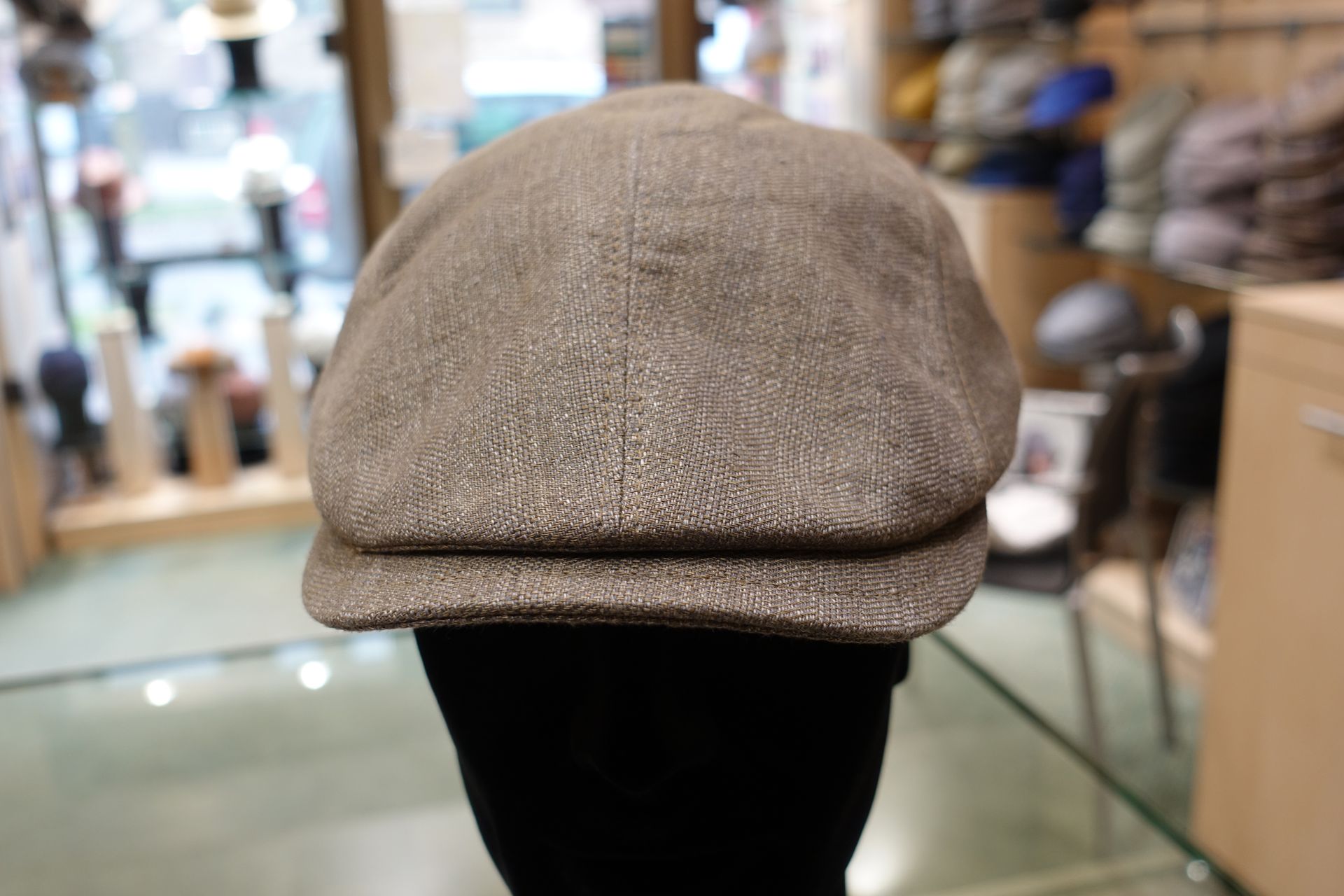 Casquette plate en laine grise présentée sur un mannequin noir dans un magasin