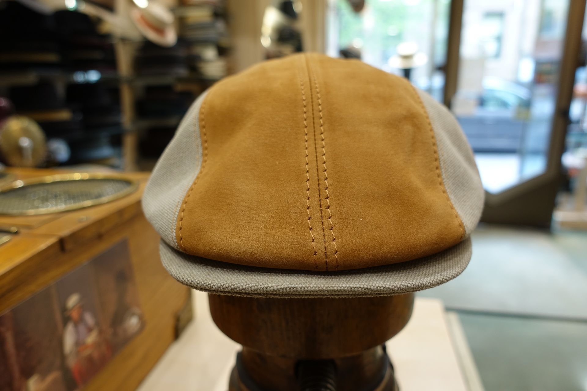 Casquette plate en daim beige avec empiècements latéraux blancs, présentée sur un présentoir en bois dans un magasin.