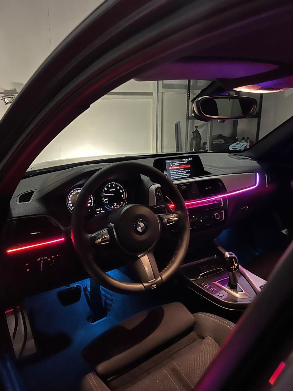 Vista interior de un BMW con iluminación ambiental LED. Se ven el volante, el salpicadero y los asientos.