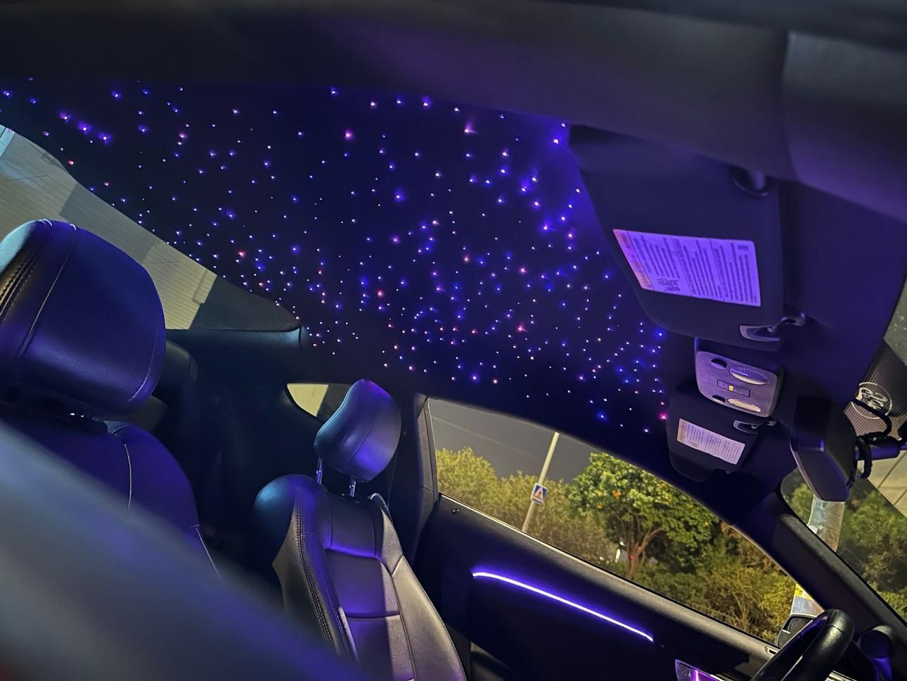 Interior del automóvil con luces de techo de noche estrellada, iluminación de acento violeta y asientos negros.