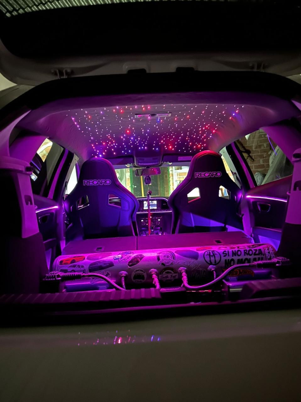Parte trasera de un coche personalizado con luces LED moradas, techo en forma de estrella y asientos de carreras.