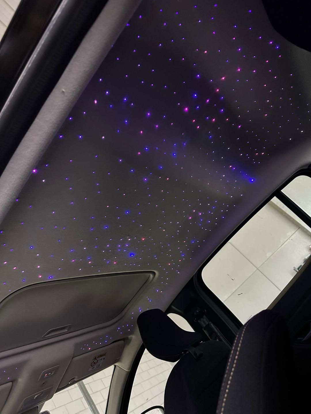 Interior de coche con techo de noche estrellada, iluminado por luces violetas y azules.