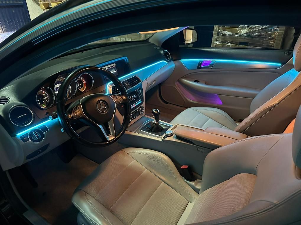 Interior del coche con iluminación ambiental azul y violeta, asientos de cuero color canela y volante negro.