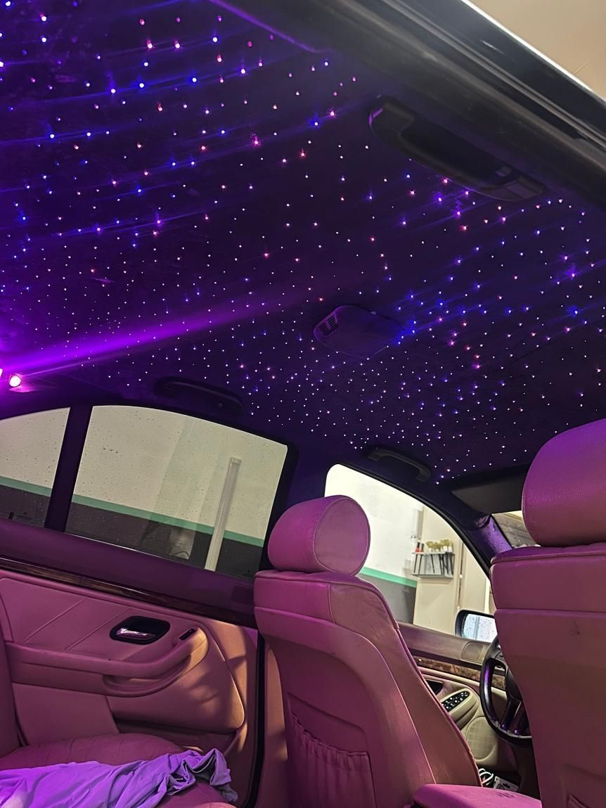 Interior del automóvil con tapizado de techo en tonos violeta, asientos color canela y una ventana lateral.