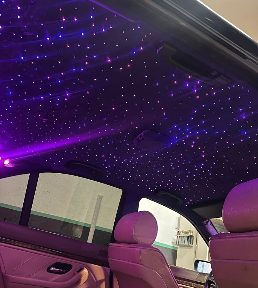 Interior del coche con luces de techo de noche estrellada de color violeta, asientos de color beige y ventanas tintadas.