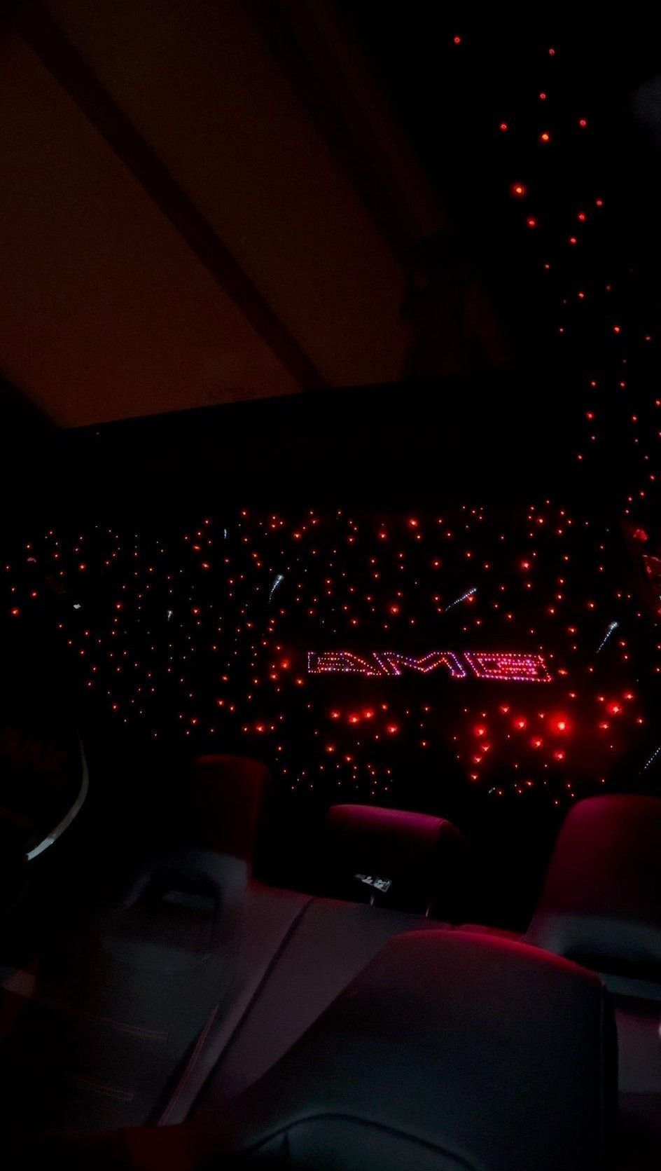 Interior del coche iluminado en rojo con un techo estrellado y una palabra brillante. Asientos visibles en primer plano.