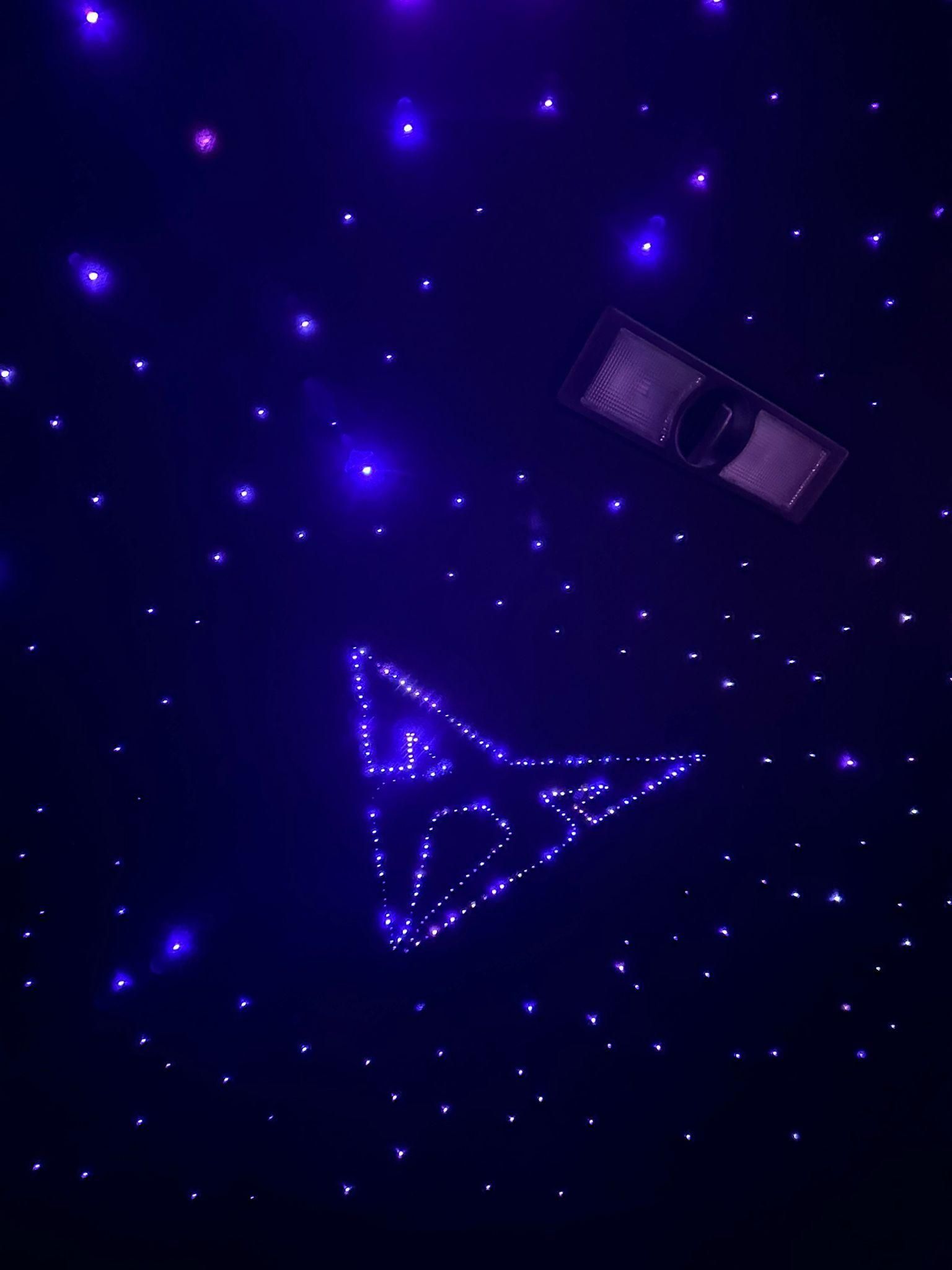Techo estrellado azul con una silueta de avión brillante y una lámpara rectangular.