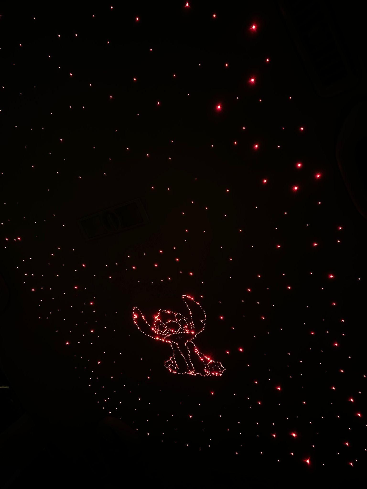 Las luces rojas delinean una figura de Stitch en un entorno oscuro, rodeada de luces rojas más pequeñas y dispersas.