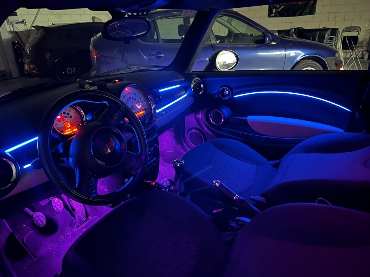 Interior de un Mini Cooper con iluminación LED morada y azul. Se ven el volante, el salpicadero y los asientos.