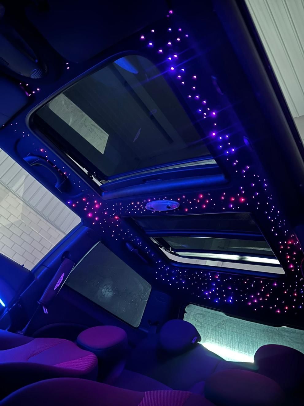 Interior del coche con efecto de noche estrellada en el techo, iluminado con luces violetas y rosas
