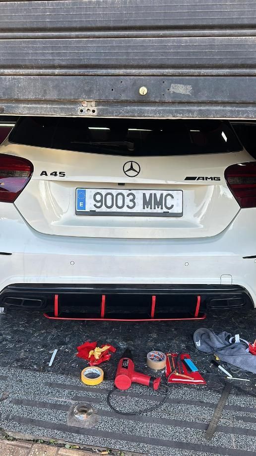 Mercedes A45 AMG blanco con matrícula española, herramientas dispuestas debajo de su parachoques para un proyecto.