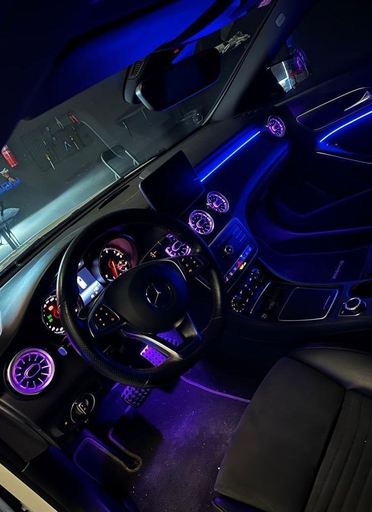 Interior de un automóvil iluminado con luces LED azules y violetas, enfocadas en el tablero y el volante.