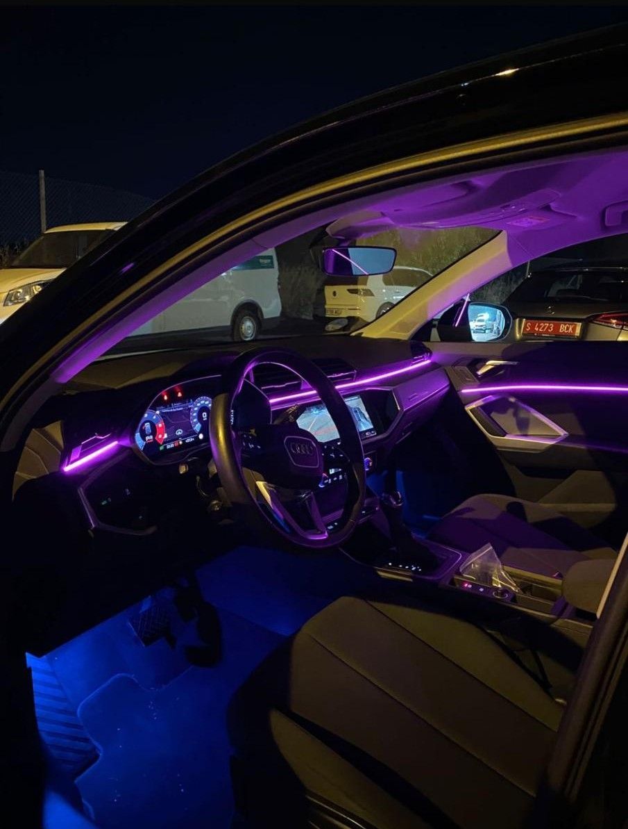 Interior de un coche de noche, iluminado con luz ambiental púrpura y azul. Volante visible.
