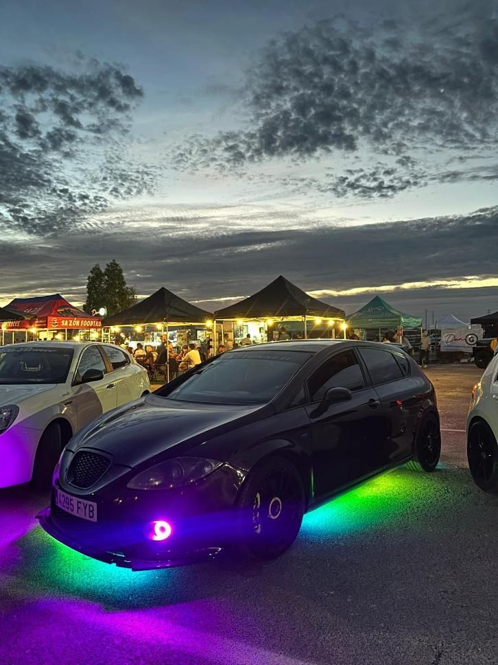 Un automóvil negro con luces incandescentes en una exhibición de automóviles, frente a un cielo nublado al anochecer.