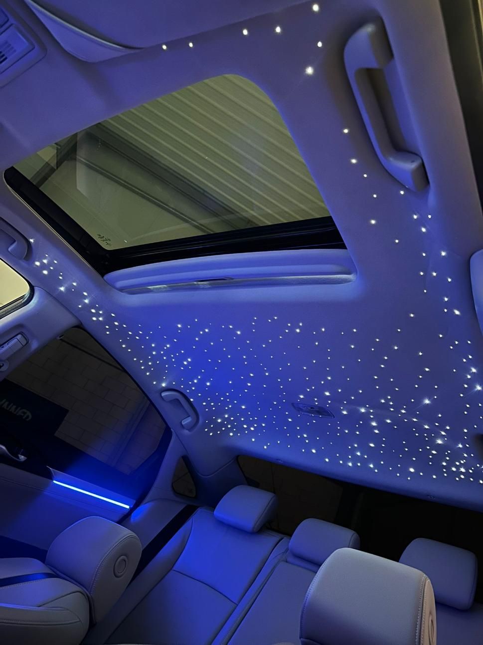 Interior del coche con iluminación de techo con efecto cielo estrellado y techo corredizo abierto. Colores azul y blanco.