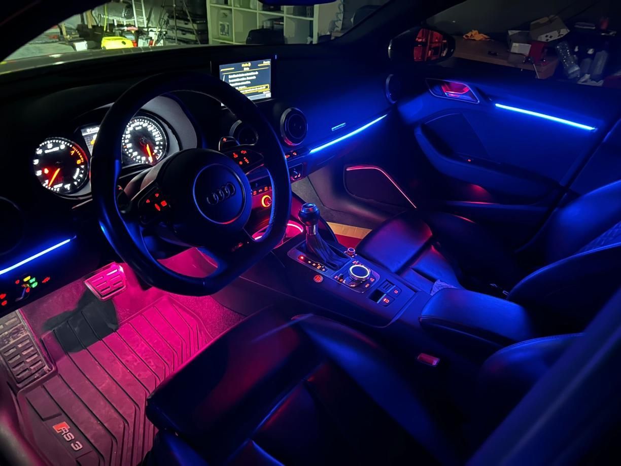 Interior de un automóvil con iluminación LED personalizada: detalles azules en el tablero y las puertas, luces de piso rosas.