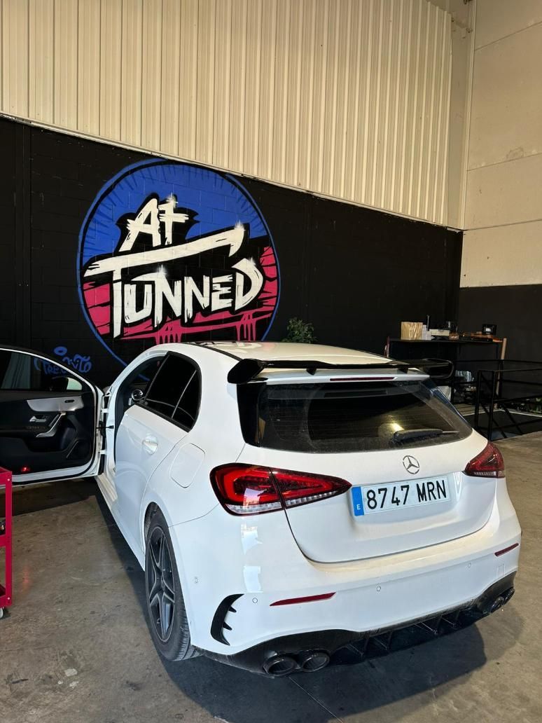 Mercedes-Benz hatchback blanco con alerón personalizado estacionado dentro de un garaje; logotipo 