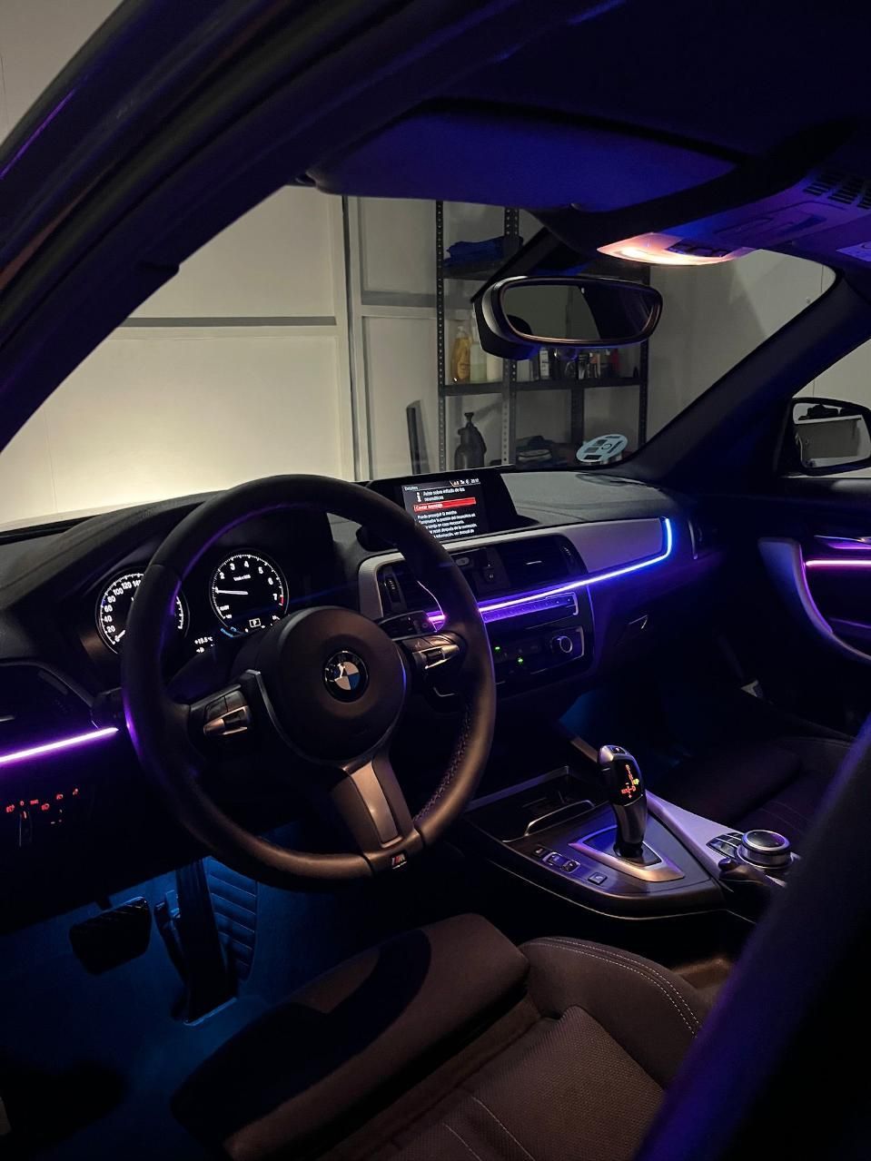 Interior del coche con iluminación ambiental violeta y azul. Se ven el volante, el salpicadero y la palanca de cambios.